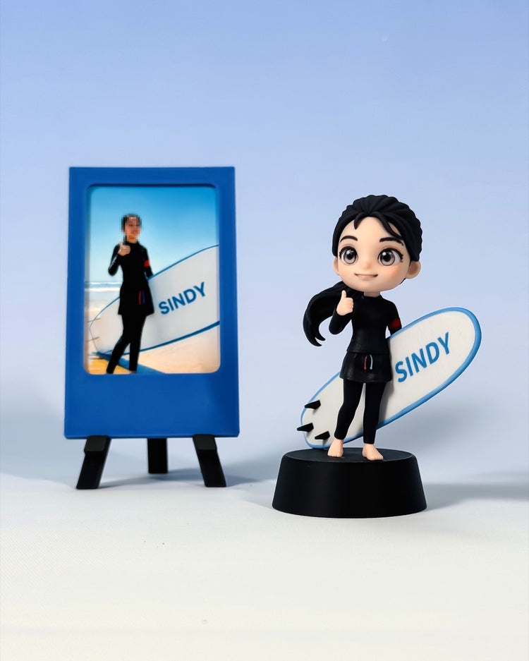Finished custom surfer figure giving a thumbs-up beside a white and blue board and simple blue photo frame