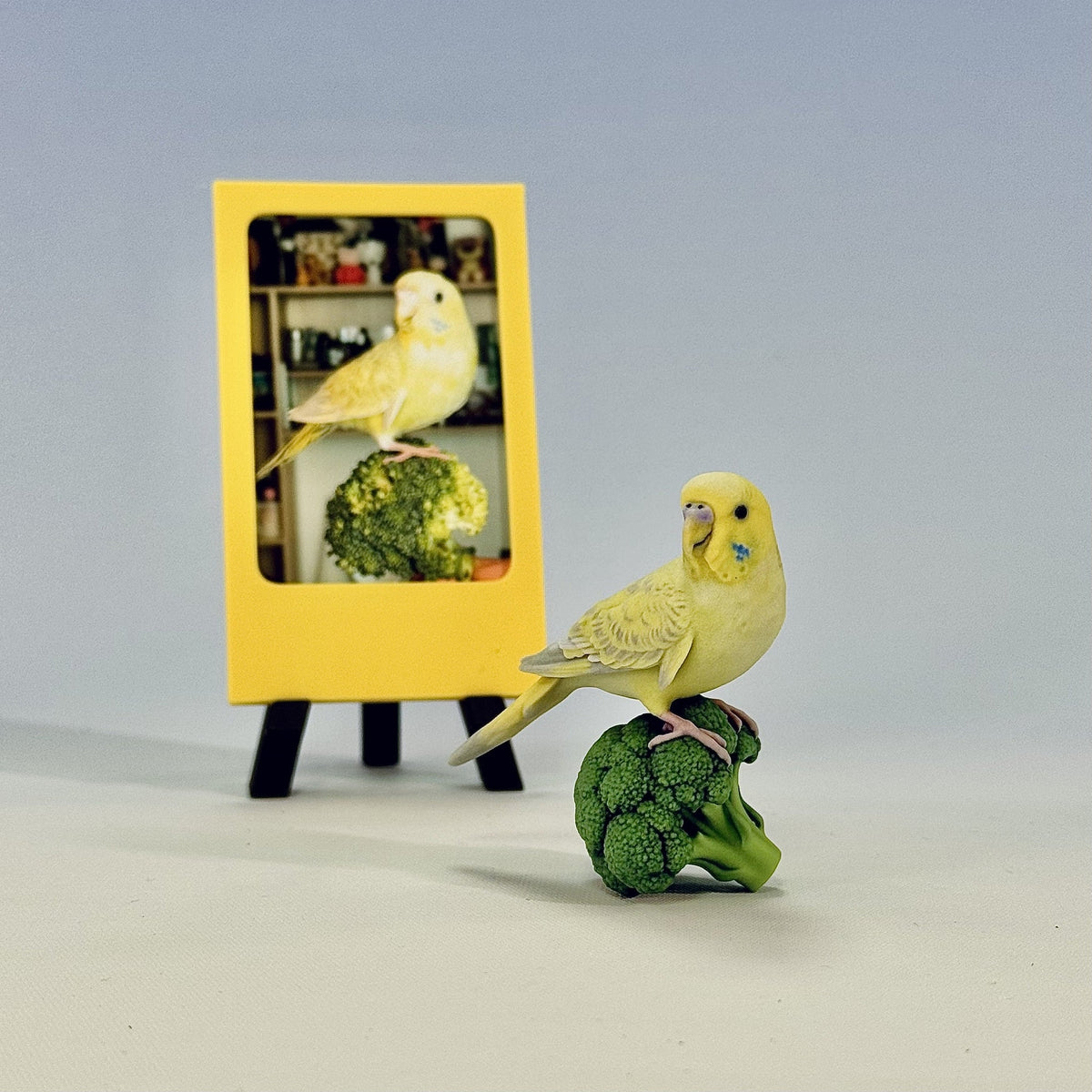 Finished custom full-color parakeet figurine beside the original pet photo