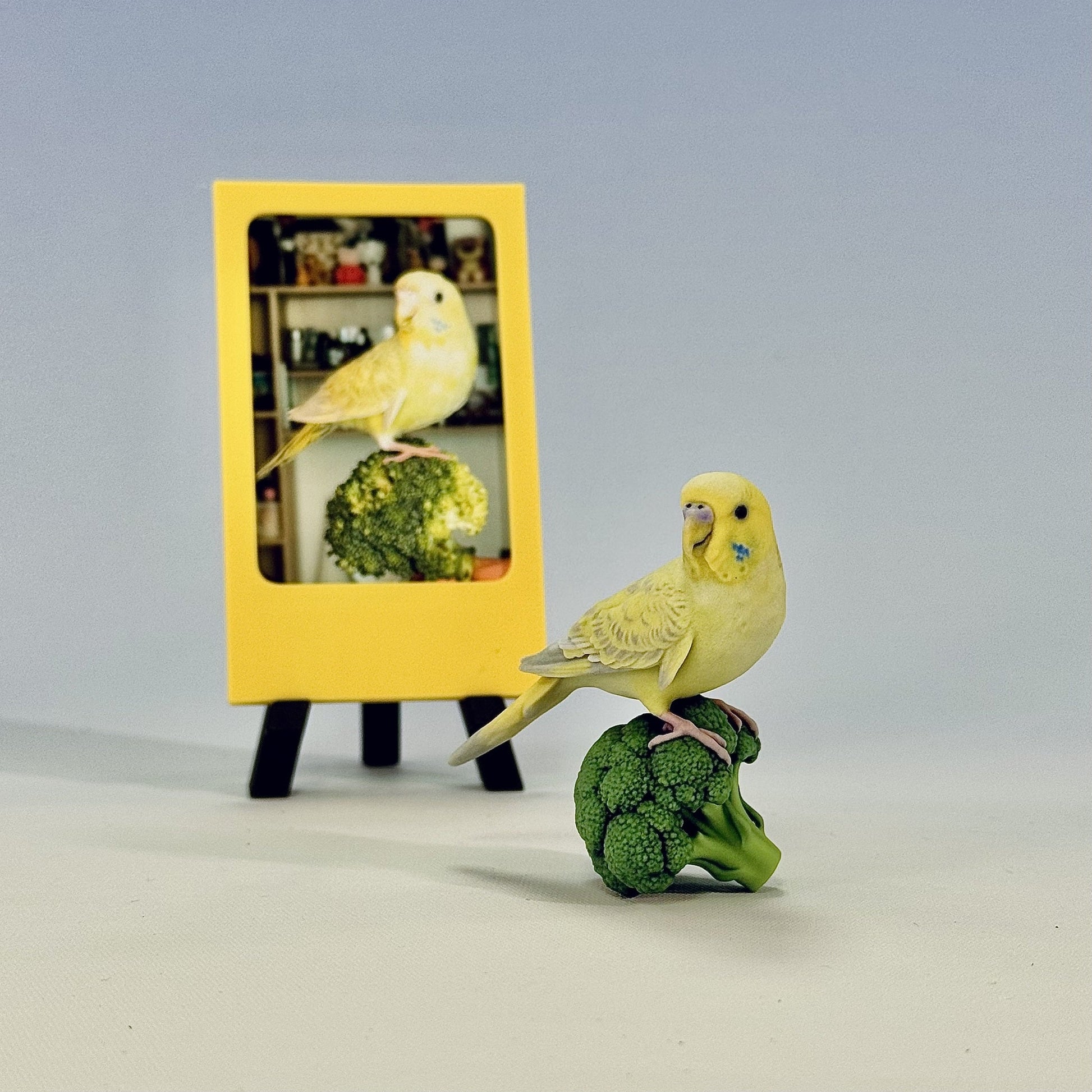 Finished custom full-color parakeet figurine beside the original pet photo