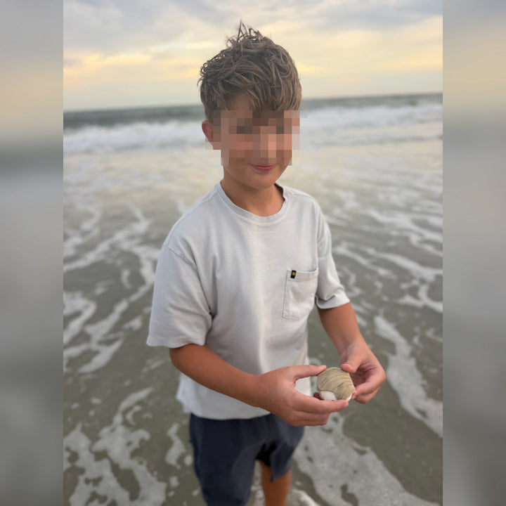 Privacy-protected reference photo of a child on a beach holding a seashell in both hands
