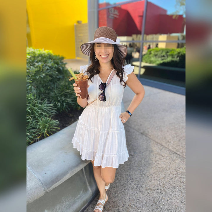 Privacy-protected reference photo of a woman in a tiered white dress and straw hat holding a drink