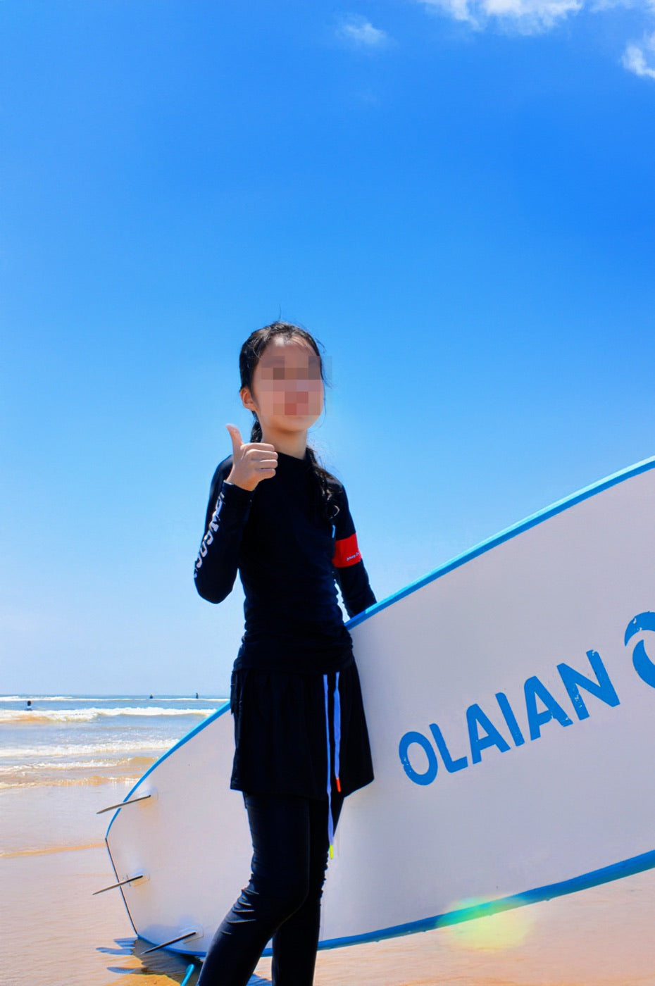 Privacy-protected reference photo of a surfer in a black outfit beside a surfboard